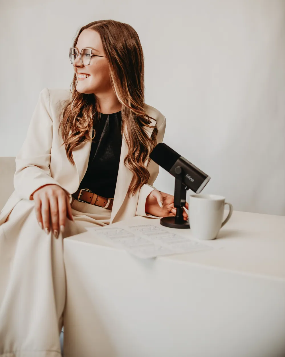 Andrea Wade seated at a white desk in a cream suit, smiling
