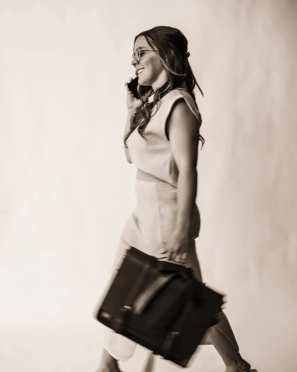 Andrea Wade walking mid-stride, phone to her ear, carrying a leather work bag