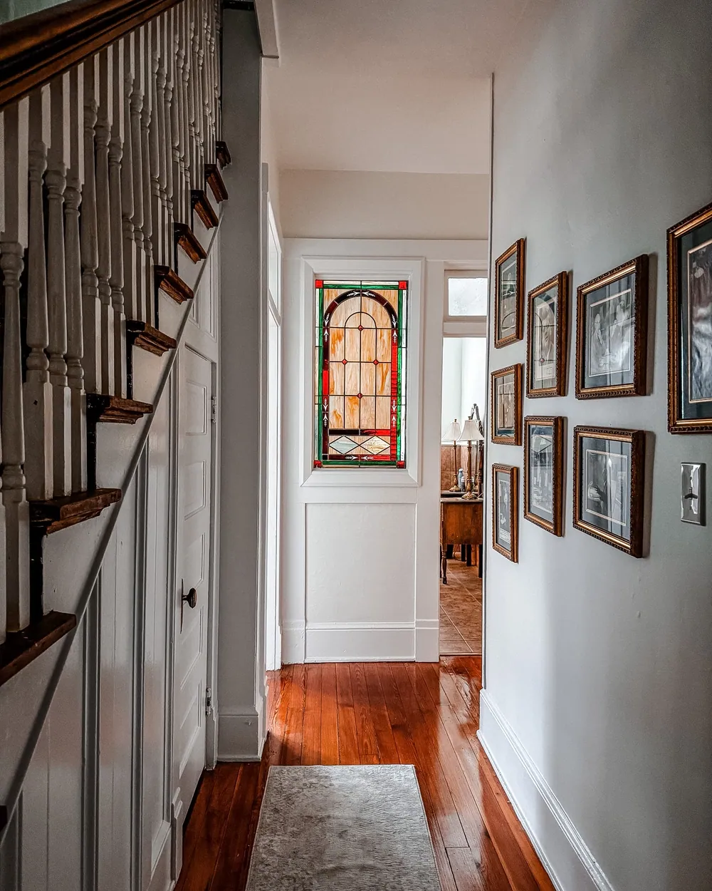 A stained glass window at the end of an interior hallway with wood floors