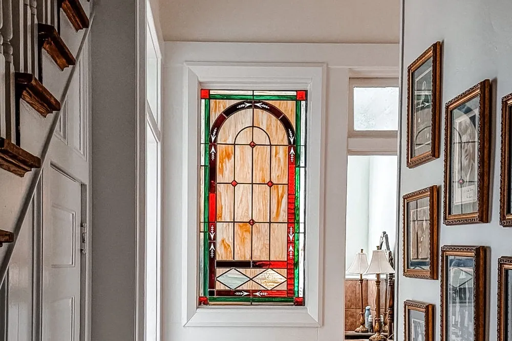A stained glass window at the end of an interior hallway with wood floors