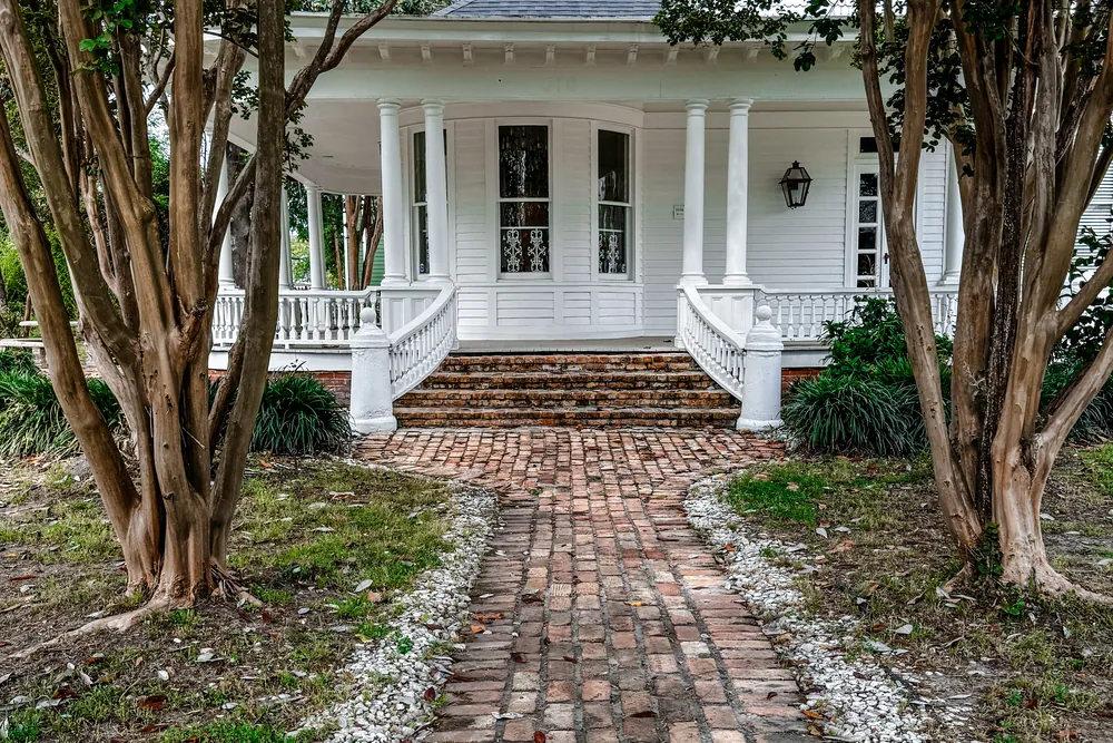 Brick walkway leading to the columned porch of a white raised cottage