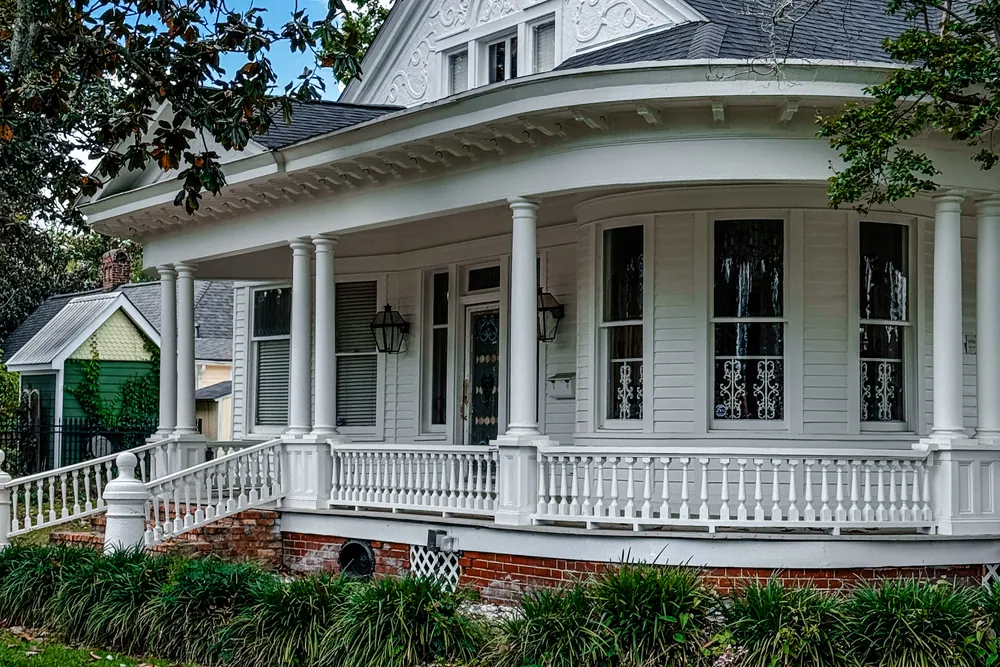 A white Louisiana home with a wraparound porch and iron railings