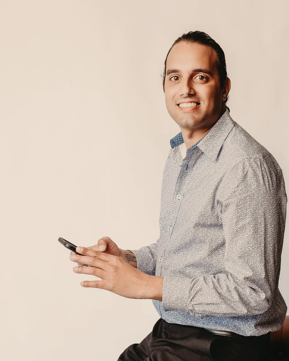Hashim Shelton seated on the arm of a leather sofa, smiling at the camera